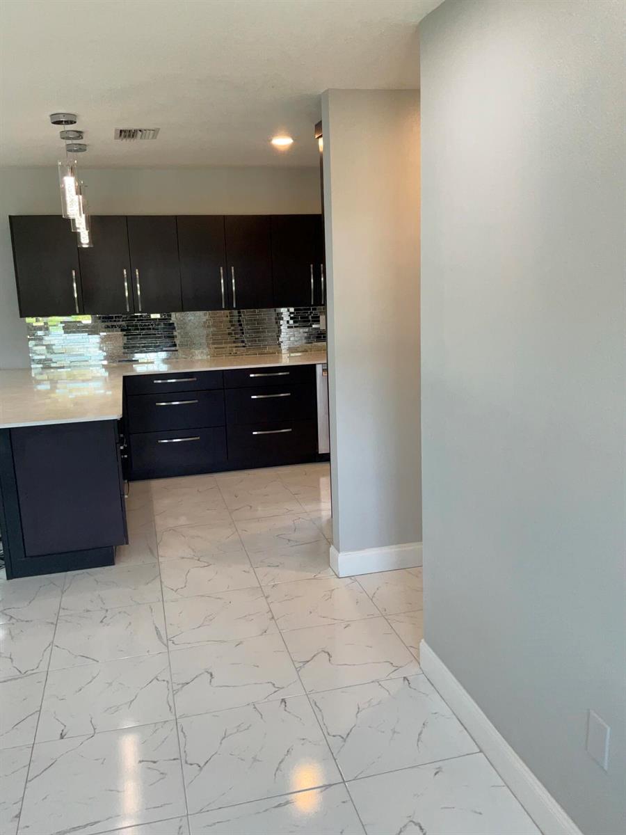 A kitchen features dark cabinetry, white countertops, a tiled backsplash, and white marble-patterned floor tiles — 300 SE 15th Avenue, Okeechobee FL 34974, OKEECHOBEE, FL
