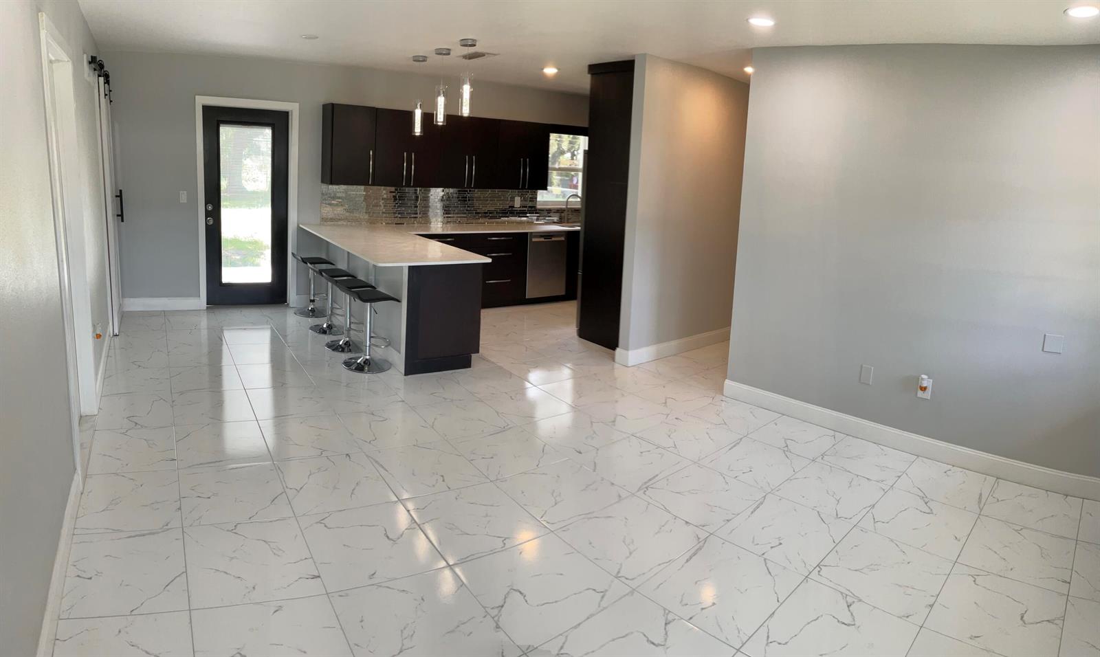 A modern kitchen features dark cabinetry, a white breakfast bar, and white marble-patterned tile flooring — 300 SE 15th Avenue, Okeechobee FL 34974, OKEECHOBEE, FL