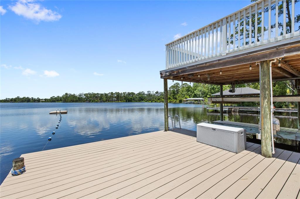A wooden dock extends over a lake beneath a two-story deck with white railings — 240 W 7TH STREET, CHULUOTA, FL