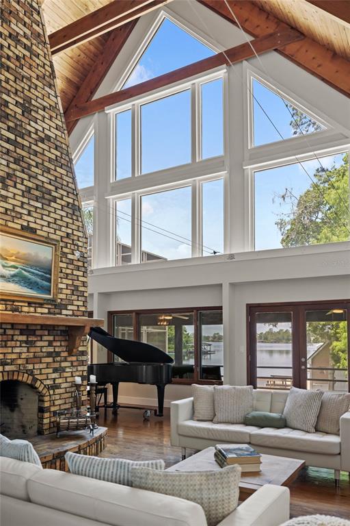 A living room features a brick fireplace, a grand piano, and floor-to-ceiling windows overlooking water — 240 W 7TH STREET, CHULUOTA, FL