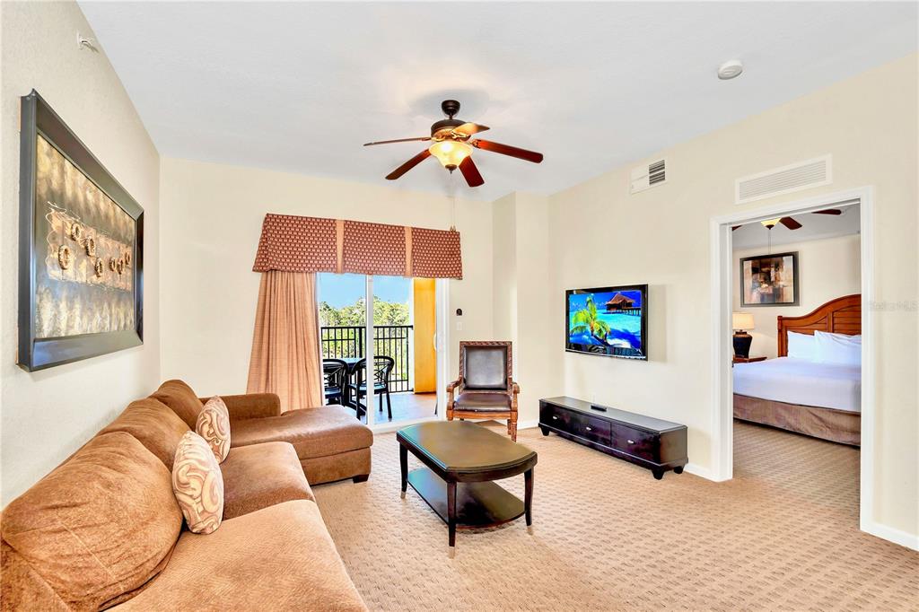 A living room features a brown sectional sofa, coffee table, television, and a balcony view — 8113 RESORT VILLAGE DRIVE UNIT 4405, ORLANDO, FL