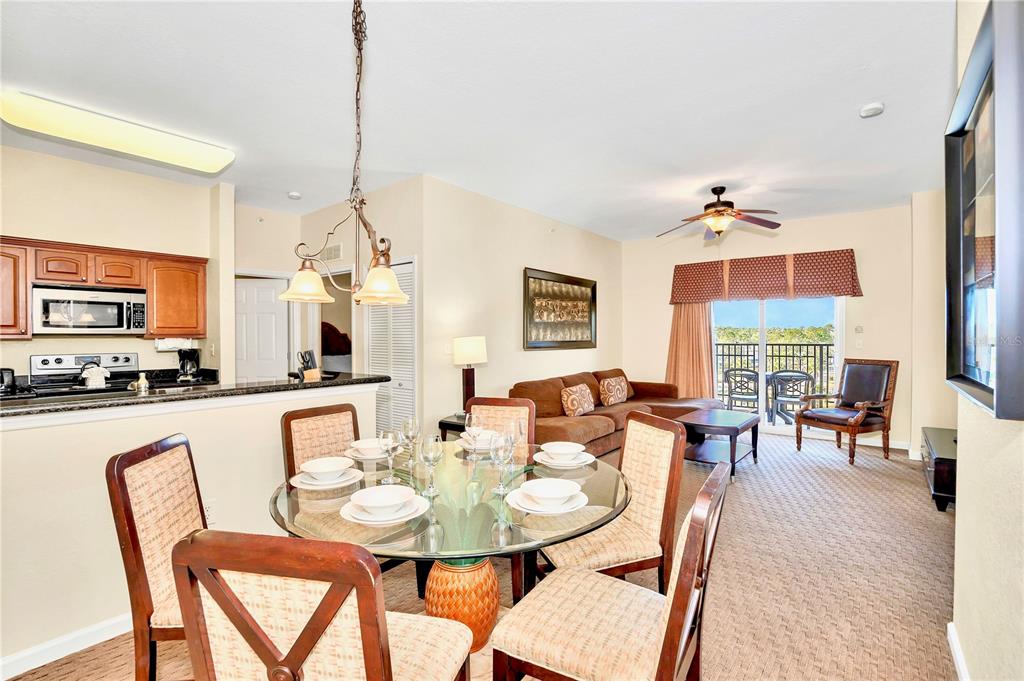 A dining area with a glass table and chairs opens to a living room with balcony — 8113 RESORT VILLAGE DRIVE UNIT 4405, ORLANDO, FL