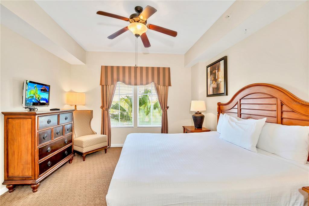 A bedroom features a king bed, wooden dresser, ceiling fan, and a window with curtains — 8113 RESORT VILLAGE DRIVE UNIT 4405, ORLANDO, FL