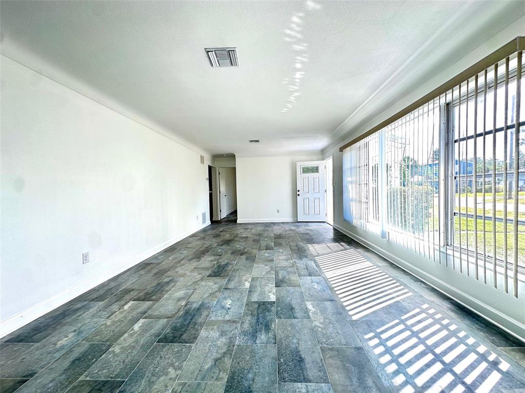 A long, empty room features gray tile flooring, white walls, and large windows with blinds — 10 158TH AVENUE, REDINGTON BEACH, FL
