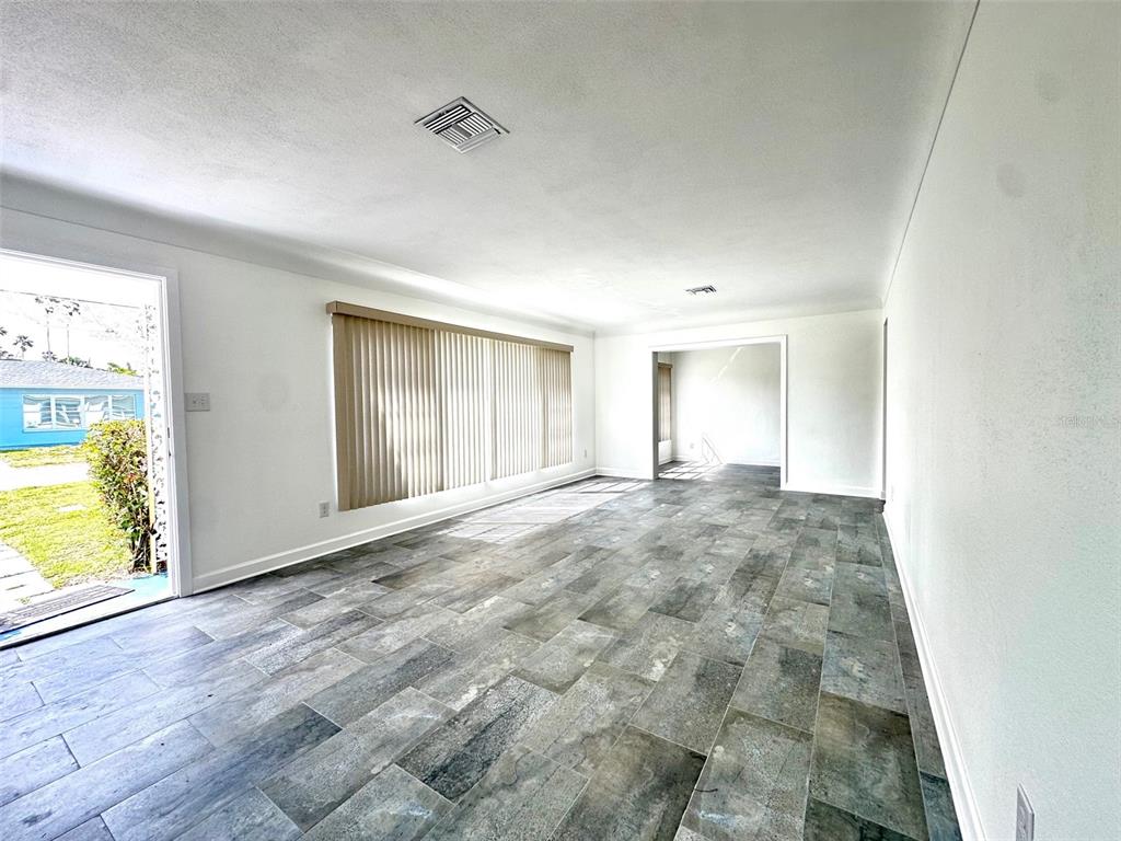 A living room with gray tile flooring, white walls, and a large window with blinds — 10 158TH AVENUE, REDINGTON BEACH, FL