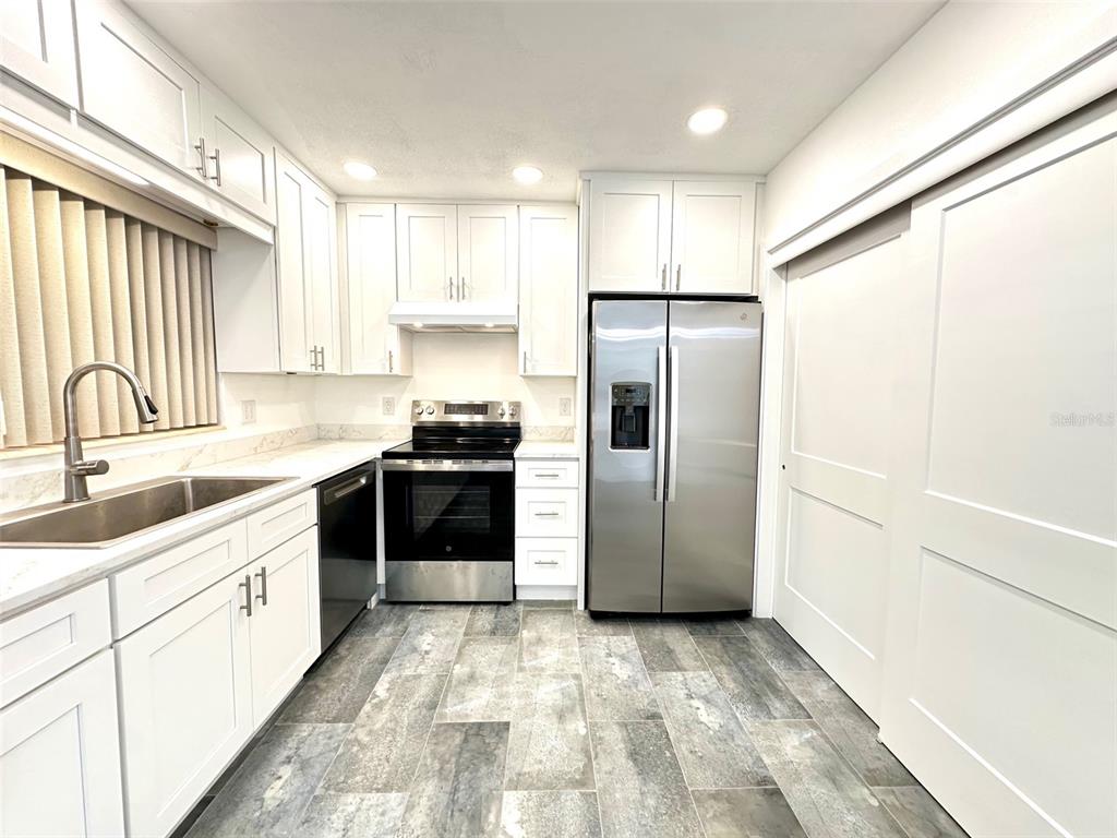 A modern kitchen features white cabinets, stainless steel appliances, and gray wood-look tile flooring — 10 158TH AVENUE, REDINGTON BEACH, FL