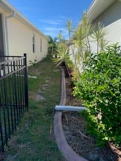 A narrow side yard features a metal fence, a concrete landscape border, and sparse landscaping — 9975 BISHOP CREEK WAY, PUNTA GORDA, FL