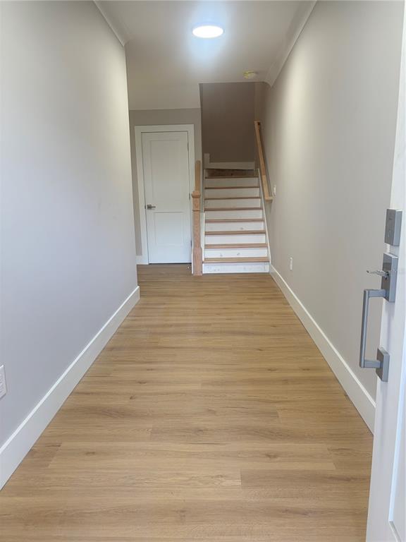 A hallway with light wood-look flooring leads to a staircase and a closed white door — 4314 W GRAY STREET, TAMPA, FL