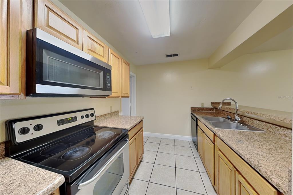 A galley kitchen features light wood cabinets, granite countertops, tile floors, and stainless steel appliances — 479 PRESTWICK PLACE, POINCIANA, FL