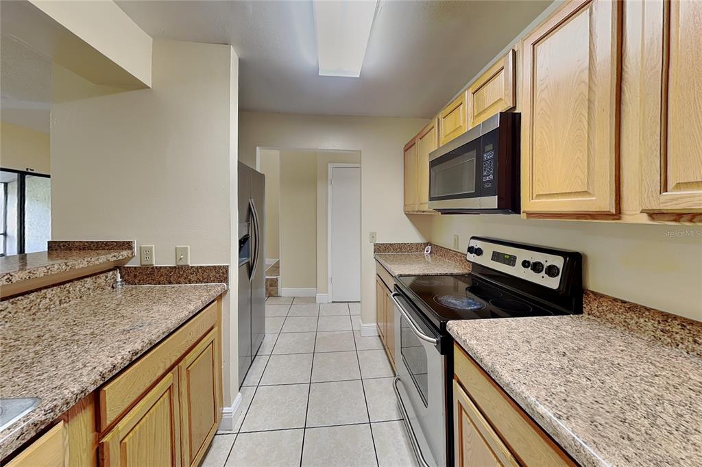 A kitchen features light wood cabinets, granite countertops, stainless steel appliances, and tiled flooring — 479 PRESTWICK PLACE, POINCIANA, FL