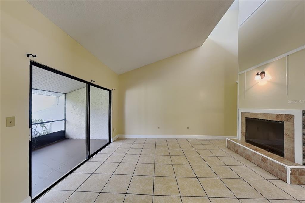 A living room with tile flooring, a fireplace, and sliding glass doors leading to a porch — 479 PRESTWICK PLACE, POINCIANA, FL