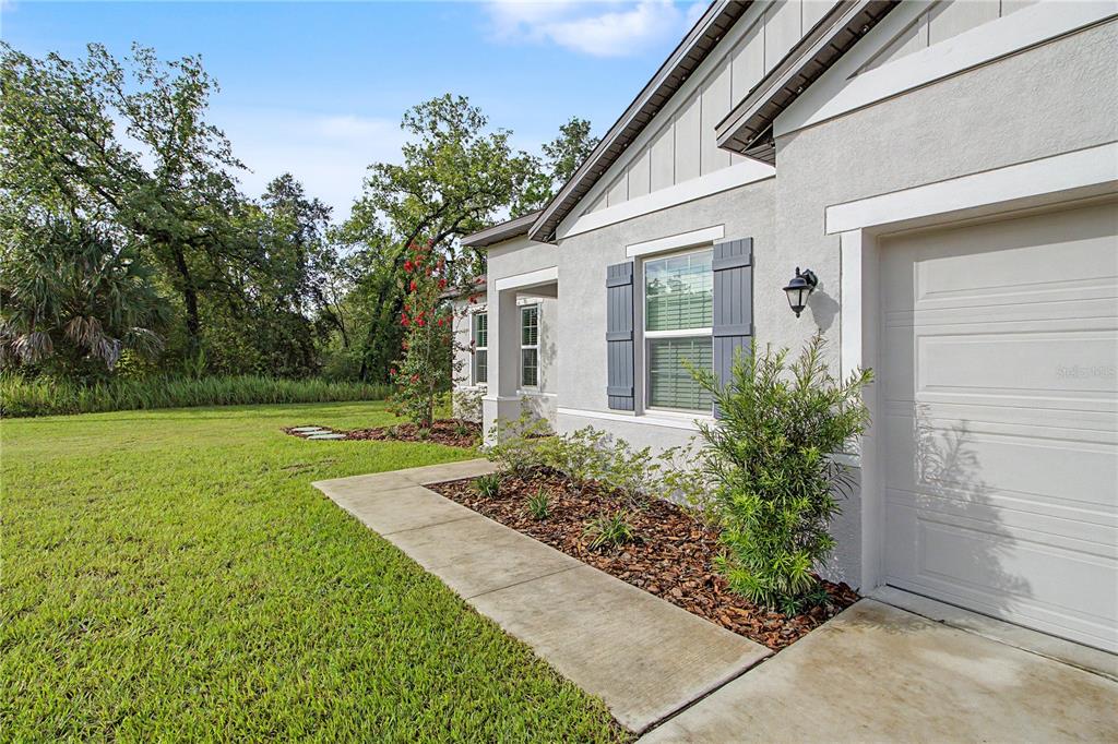 A side view of a light-colored house exterior featuring a garage, window shutters, and landscaping — 14557 CEDARWOOD AVENUE, WEEKI WACHEE, FL