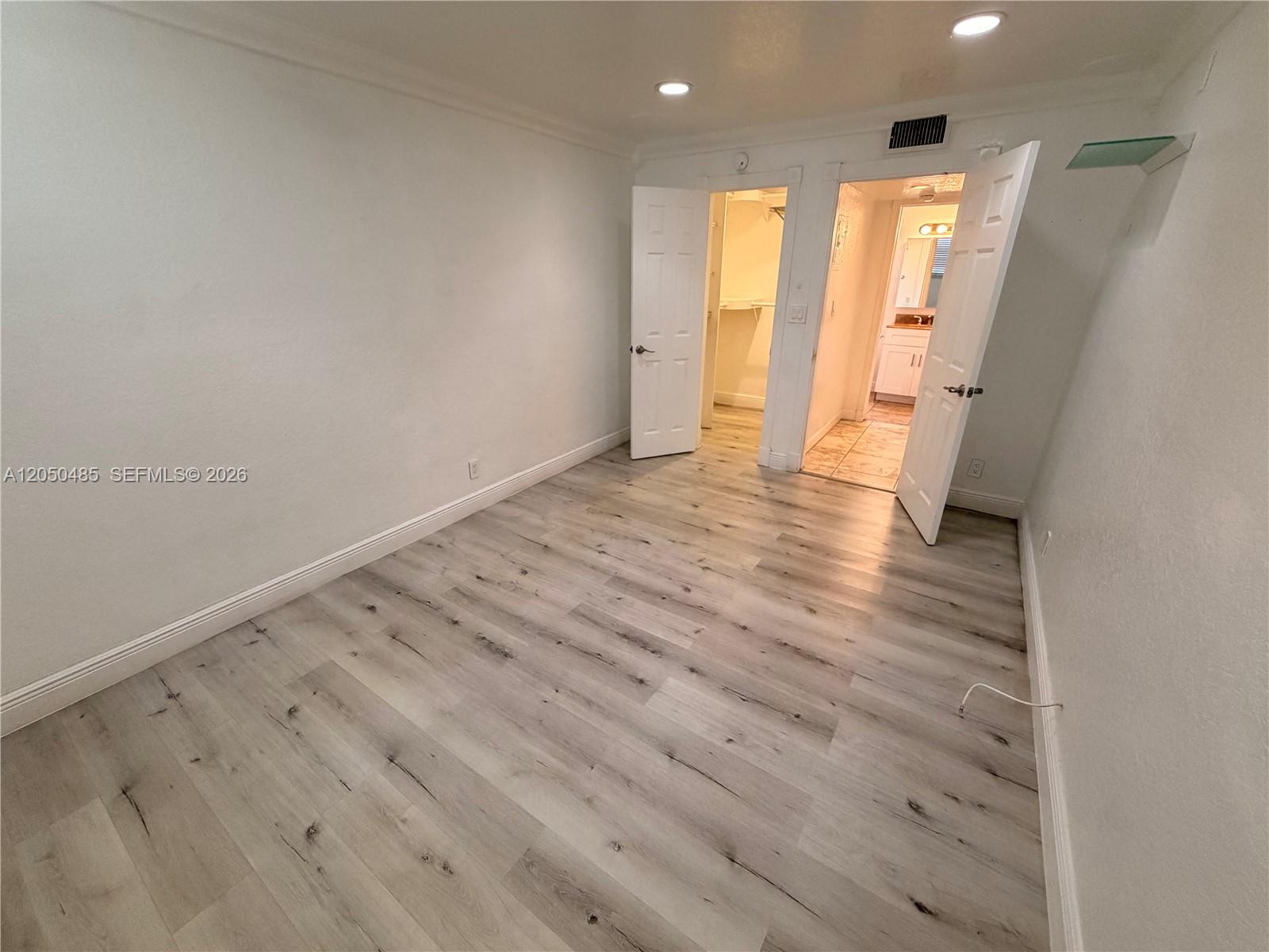 An empty bedroom features light wood-look flooring, white walls, recessed lighting, and an attached bathroom — 2826 Van Buren St # 2, Hollywood FL 33020, HOLLYWOOD, FL