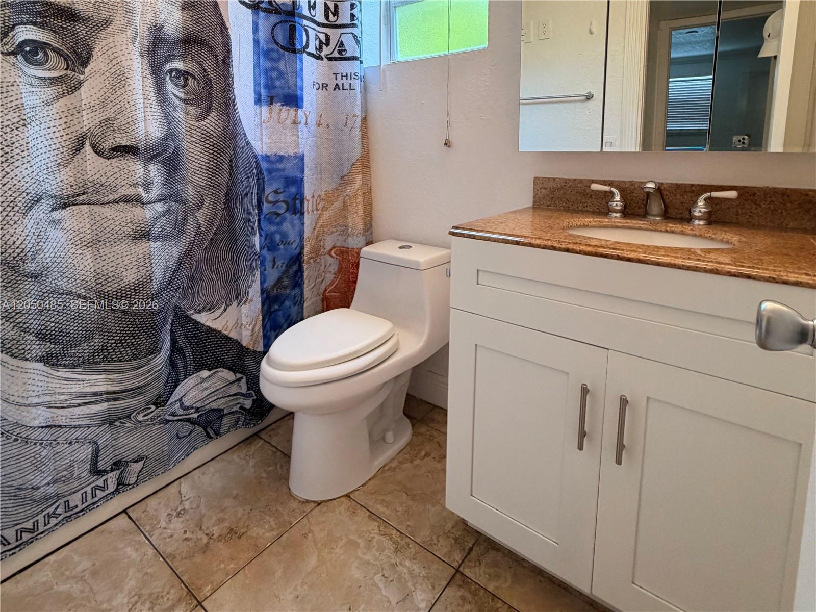 A bathroom features a money-themed shower curtain, a white toilet, and a granite-topped vanity — 2826 Van Buren St # 2, Hollywood FL 33020, HOLLYWOOD, FL