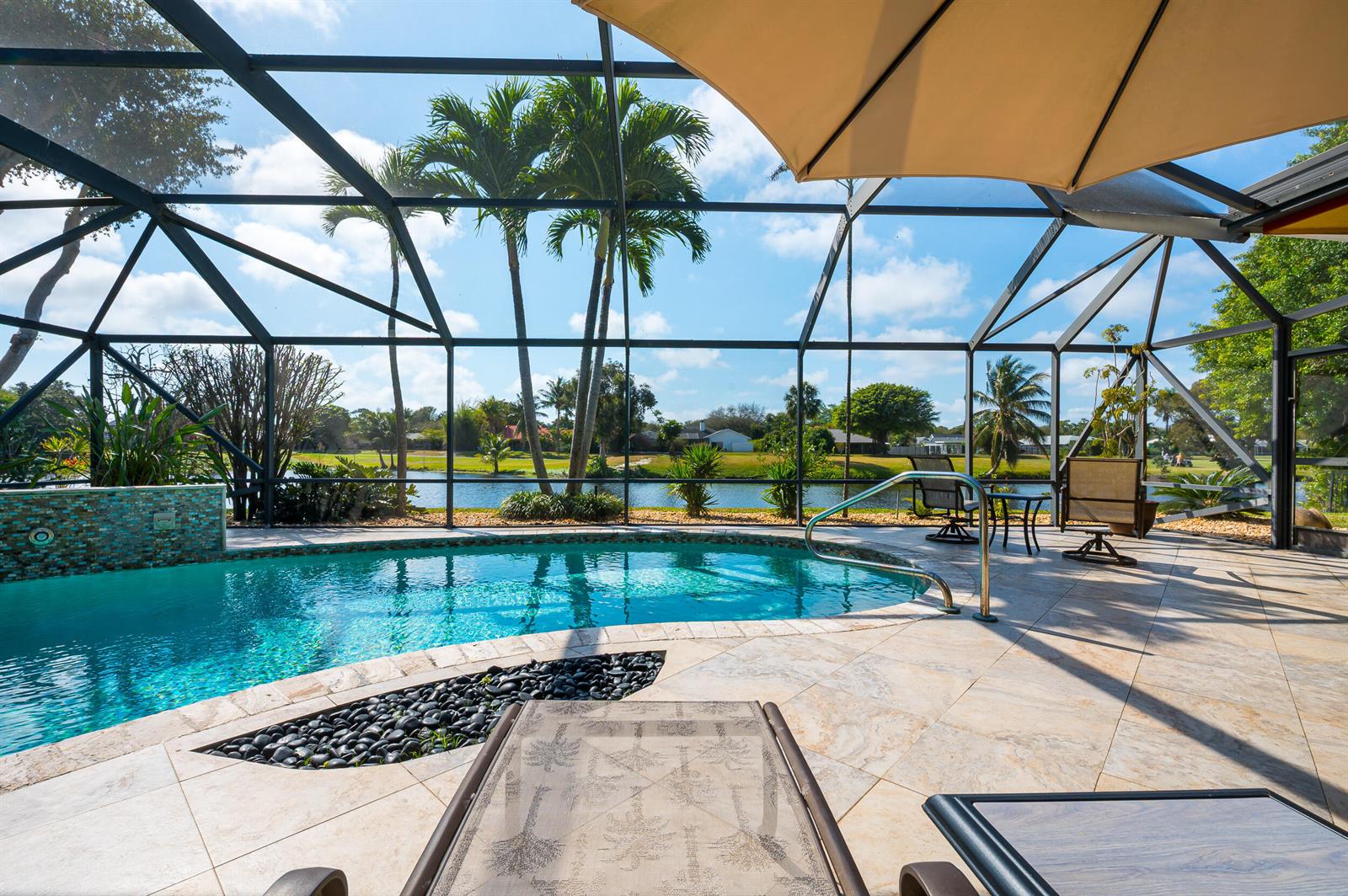 A screened-in pool patio features a swimming pool, lounge chairs, and a view of a lake — 3250 Lakeview Boulevard, Delray Beach FL 33445, DELRAY BEACH, FL