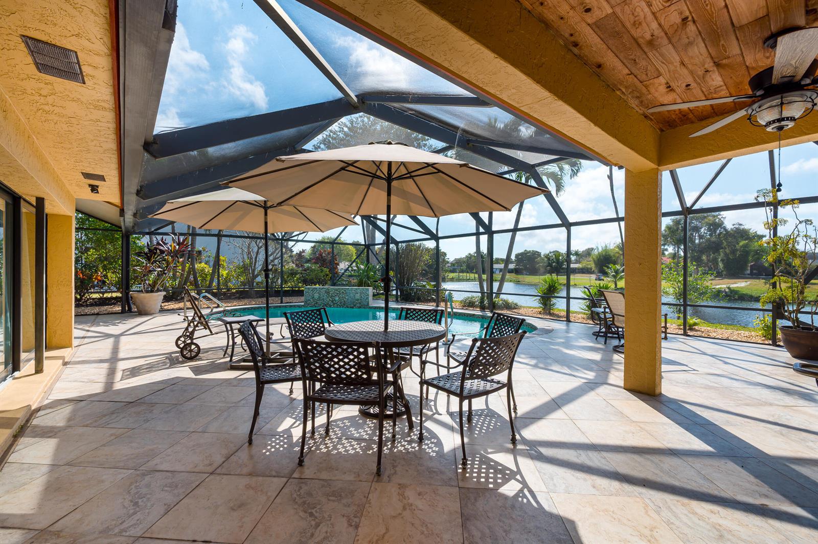 A covered patio features a dining set, pool, and screen enclosure overlooking a lake — 3250 Lakeview Boulevard, Delray Beach FL 33445, DELRAY BEACH, FL