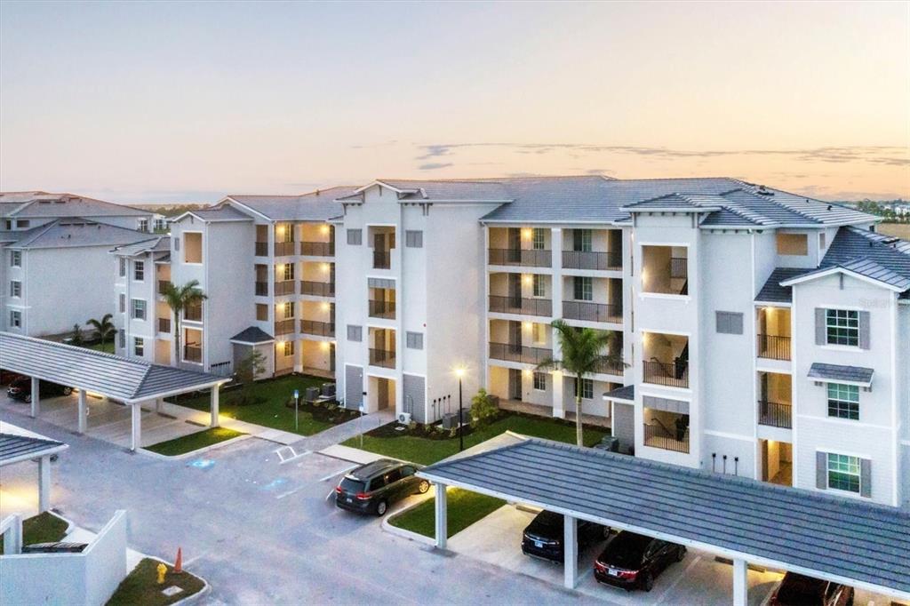 An aerial view of a multi-story apartment complex with covered parking and palm trees — 12140 WELLEN GOLF STREET UNIT 404, VENICE, FL
