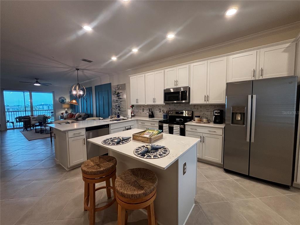 A kitchen features white cabinets, stainless steel appliances, a central island, and tile flooring — 12140 WELLEN GOLF STREET UNIT 404, VENICE, FL