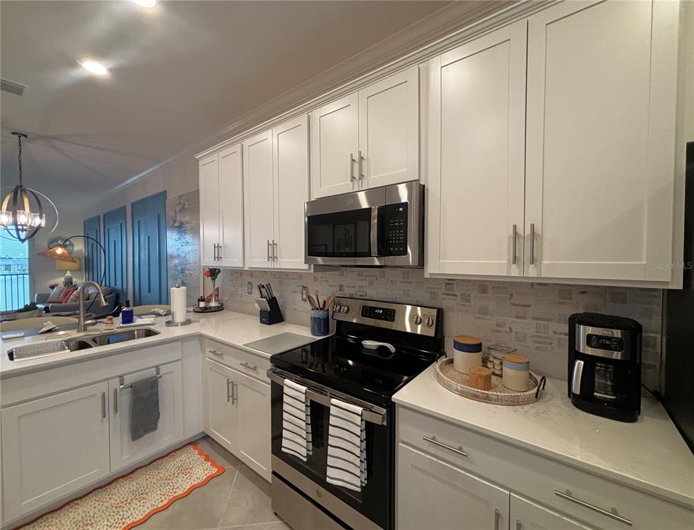 A kitchen features white cabinetry, stainless steel appliances, a tiled backsplash, and light-colored countertops — 12140 WELLEN GOLF STREET UNIT 404, VENICE, FL
