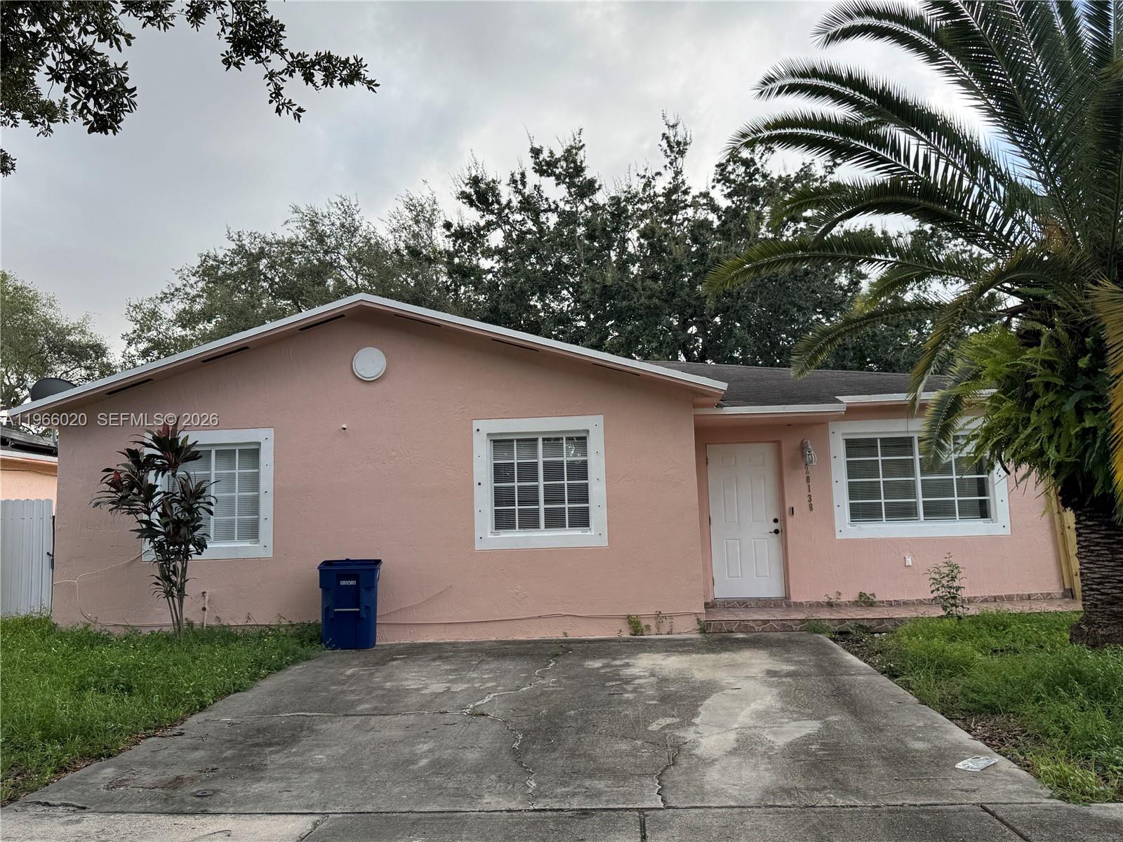 A single-story pink house with a concrete driveway and a palm tree in the yard — 20138 NW 38th Pl, Miami Gardens FL 33055, MIAMI GARDENS, FL