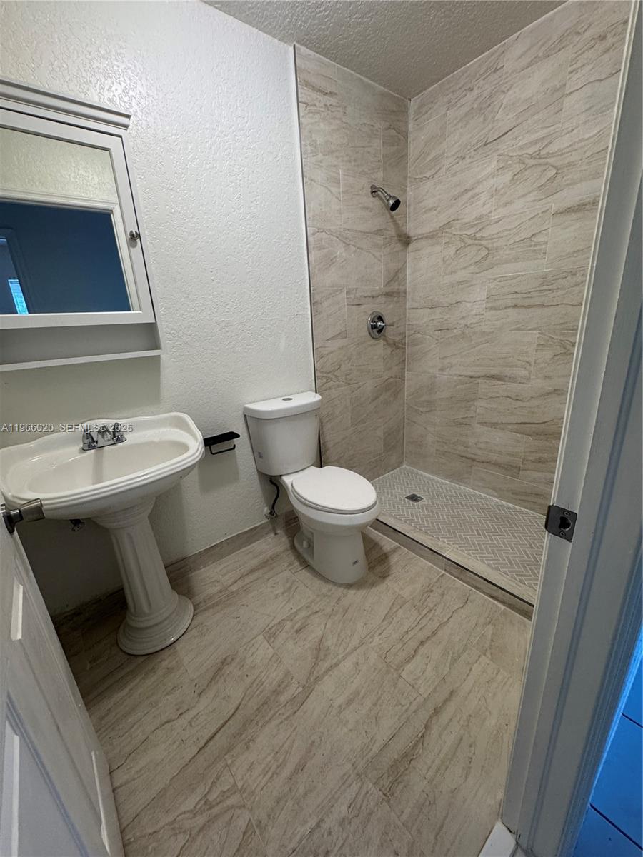 A bathroom features a pedestal sink, a toilet, and a walk-in shower with tiled walls — 20138 NW 38th Pl, Miami Gardens FL 33055, MIAMI GARDENS, FL