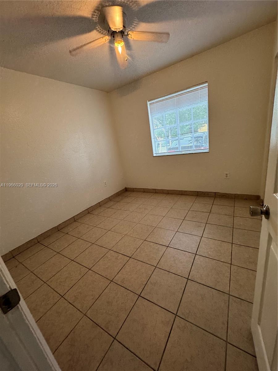An empty bedroom features beige tile flooring, a ceiling fan, and a single window — 20138 NW 38th Pl, Miami Gardens FL 33055, MIAMI GARDENS, FL