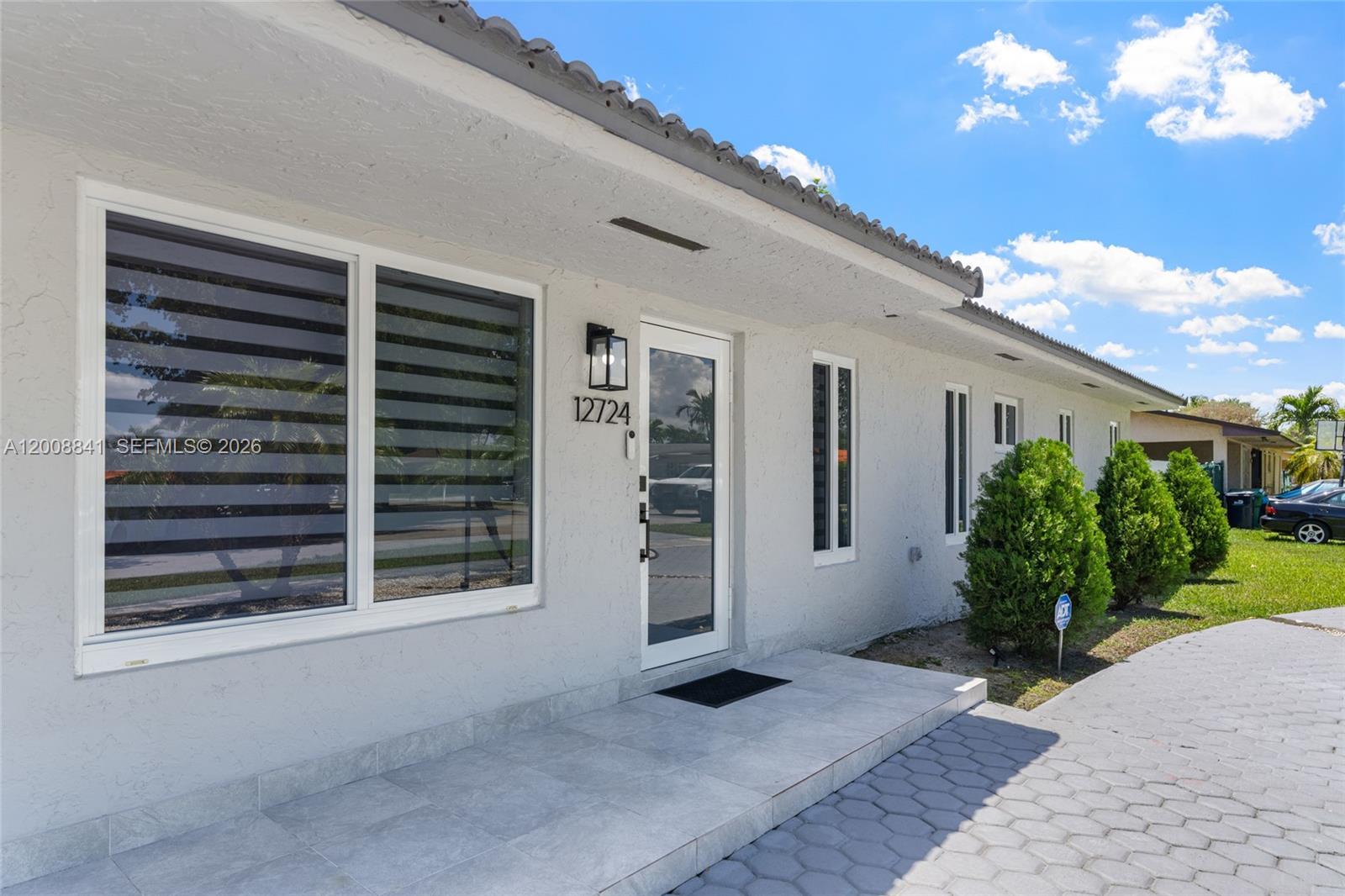 The exterior of a light-colored house features a tiled porch, a glass door, and windows — 12724 SW 33rd Ter, Miami FL 33175, MIAMI, FL