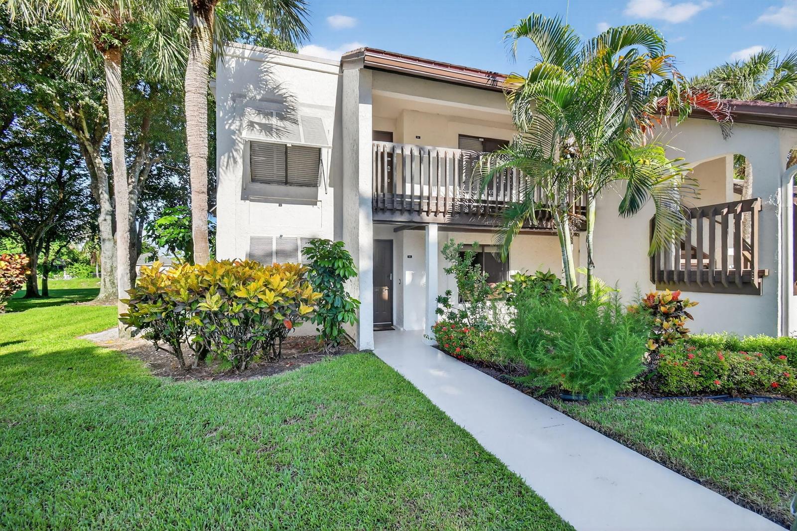 A two-story residential building with a balcony, a concrete walkway, and surrounding tropical landscaping — 10155 Mangrove Drive # 101, Boynton Beach FL 33437, BOYNTON BEACH, FL