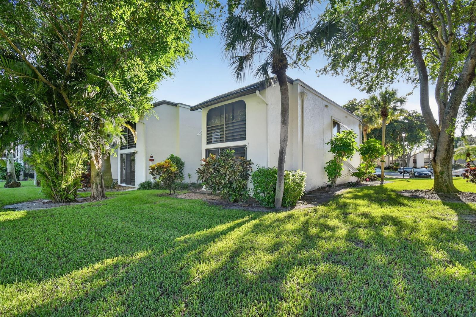 Exterior view of two-story white stucco apartment buildings surrounded by lush green trees and grass — 10155 Mangrove Drive # 101, Boynton Beach FL 33437, BOYNTON BEACH, FL