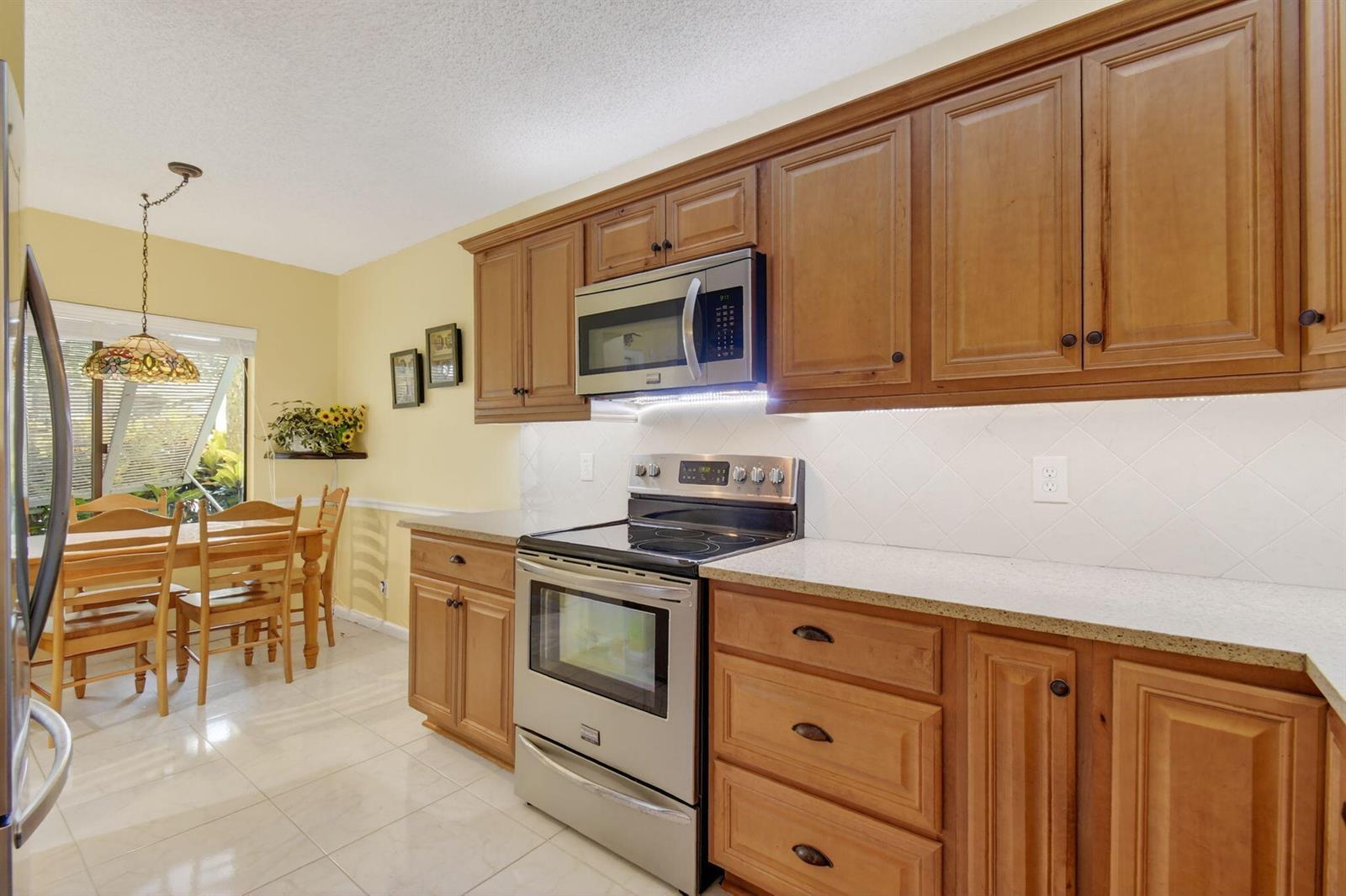 A kitchen with wood cabinets, stainless steel appliances, and a dining area with a window — 10155 Mangrove Drive # 101, Boynton Beach FL 33437, BOYNTON BEACH, FL