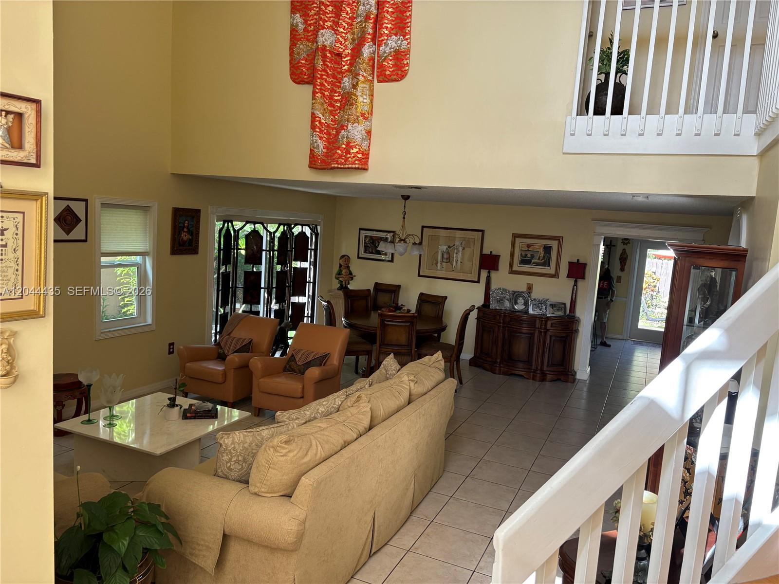 A high-ceilinged living and dining area features tile floors, a tan sofa, and a kimono — 9217 SW 157th Path, Miami FL 33196, MIAMI, FL