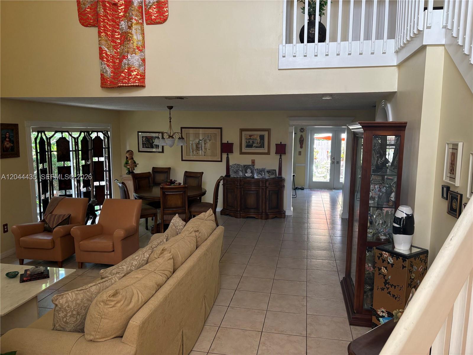 A high-ceilinged living and dining area features tiled floors, a sofa, and a display cabinet — 9217 SW 157th Path, Miami FL 33196, MIAMI, FL