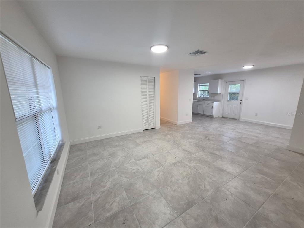 An open-concept living area features light gray tile flooring, white walls, and an adjacent kitchen — 5907 NW 64TH STREET, OCALA, FL