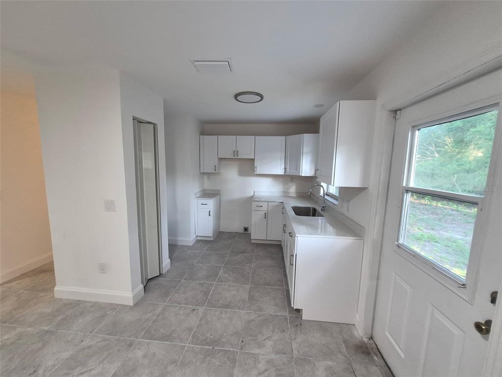 A kitchen features white cabinets, light countertops, a stainless steel sink, and gray tile flooring — 5907 NW 64TH STREET, OCALA, FL