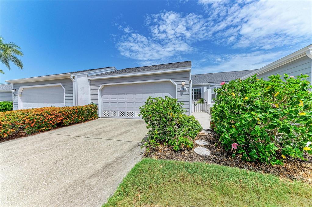 A single-story house exterior features a gray garage, a concrete driveway, and landscaped bushes — 1218 SPOONBILL LANDINGS CIR, BRADENTON, FL