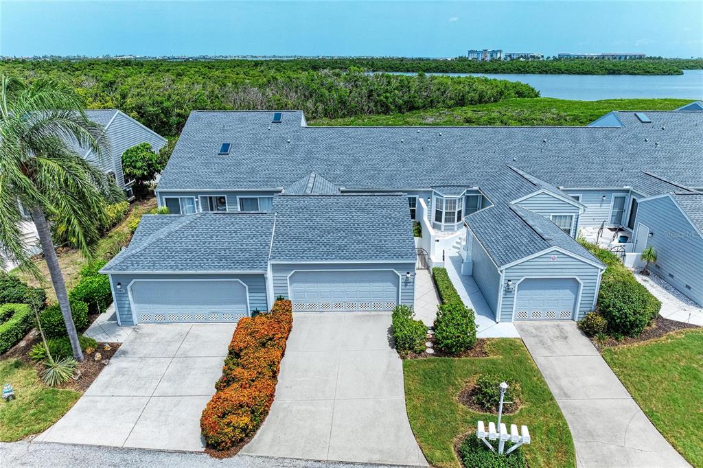 An aerial view shows a multi-unit residential building with gray siding, shingled roofs, and driveways — 1218 SPOONBILL LANDINGS CIR, BRADENTON, FL