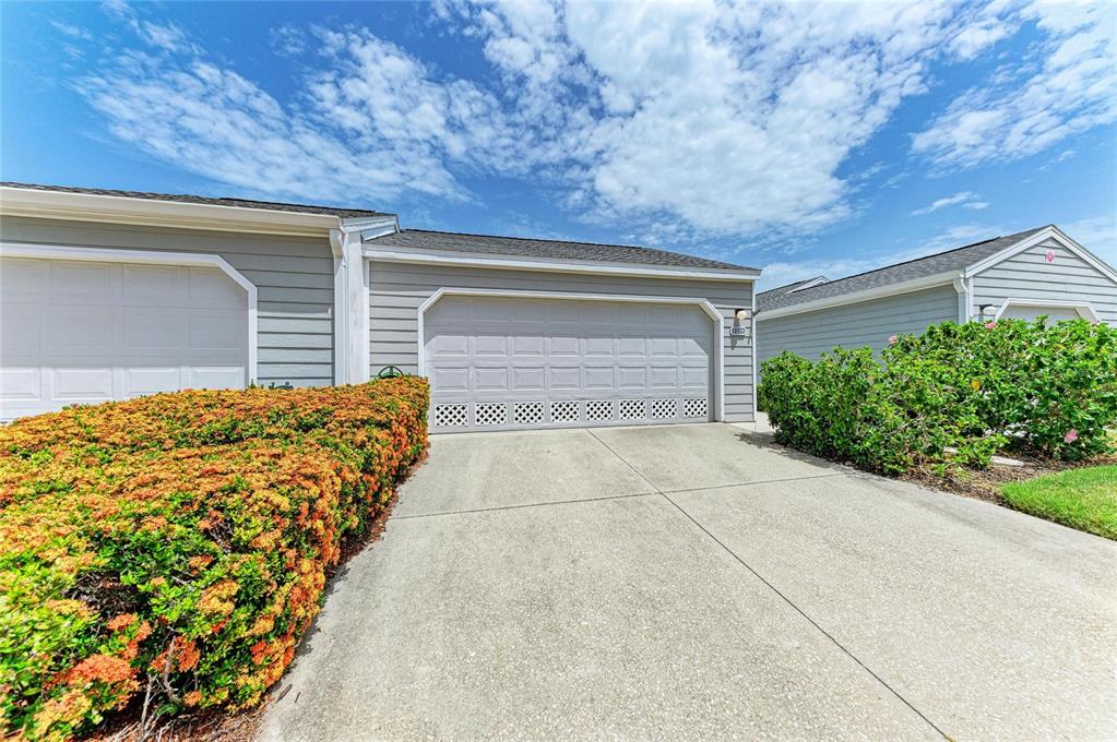 A gray garage with a concrete driveway and a large hedge in the foreground — 1218 SPOONBILL LANDINGS CIR, BRADENTON, FL