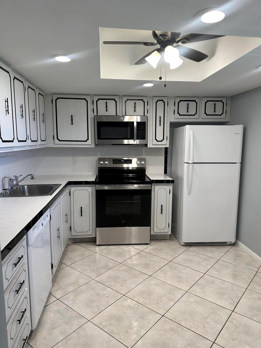 A kitchen features white cabinets with black trim, stainless steel appliances, and tiled countertops — 2600 NE 1st Lane # 418, Boynton Beach FL 33435, BOYNTON BEACH, FL