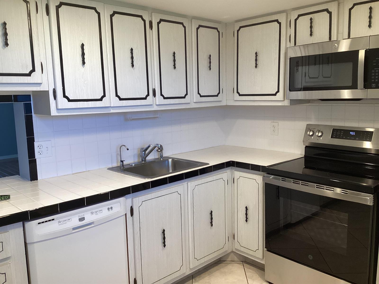 A kitchen with white wood-grain cabinets, black trim, white tile countertops, and stainless steel appliances — 2600 NE 1st Lane # 418, Boynton Beach FL 33435, BOYNTON BEACH, FL
