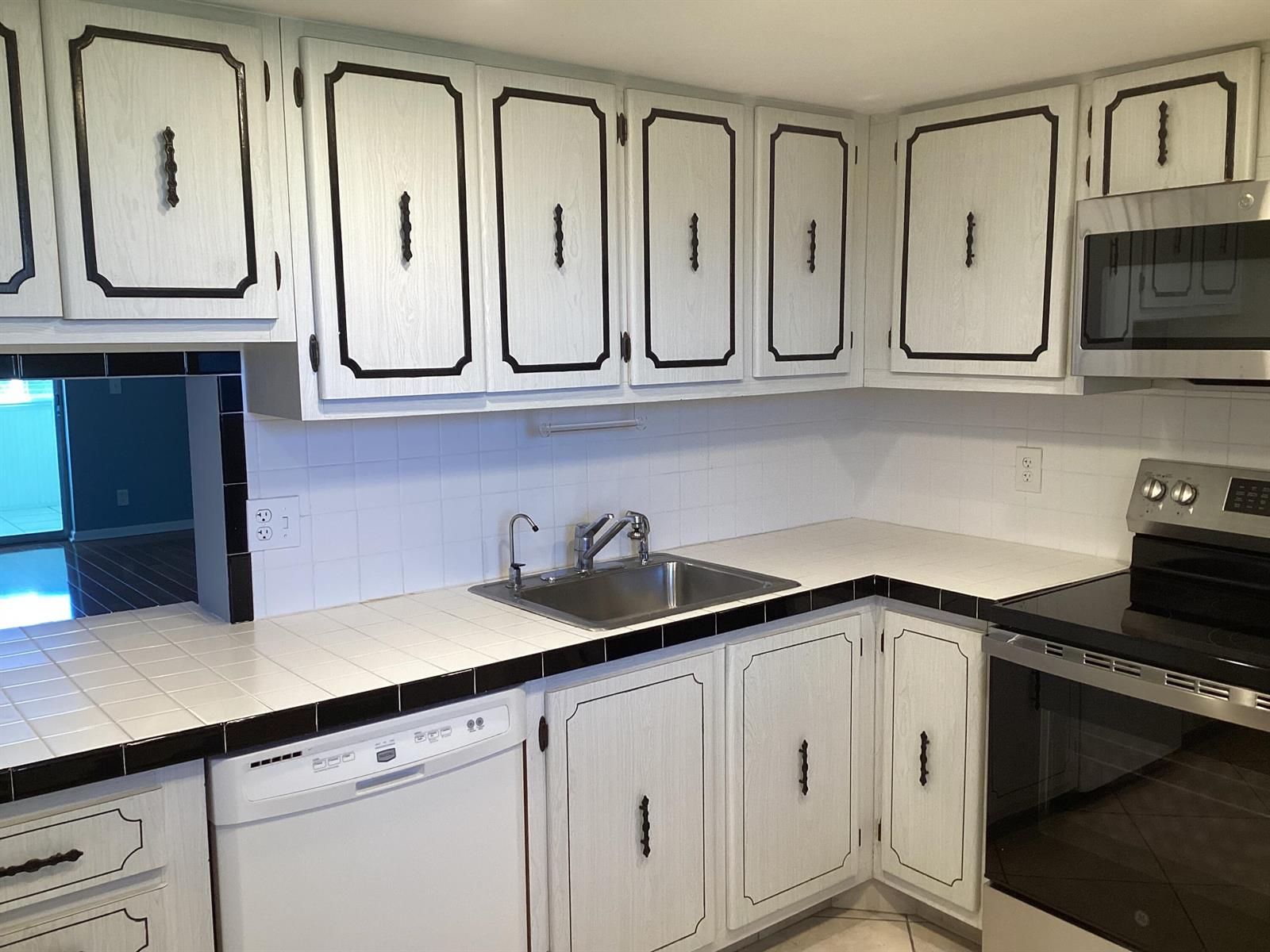A kitchen features white cabinets with black trim, a tile countertop, and stainless steel appliances — 2600 NE 1st Lane # 418, Boynton Beach FL 33435, BOYNTON BEACH, FL