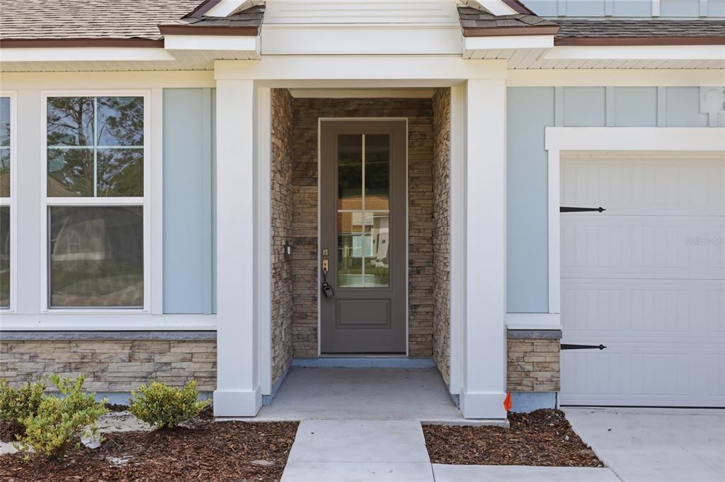 A front entrance with a glass-paneled door, stone siding, and white columns — 14 PROSPECT LANE, PALM COAST, FL