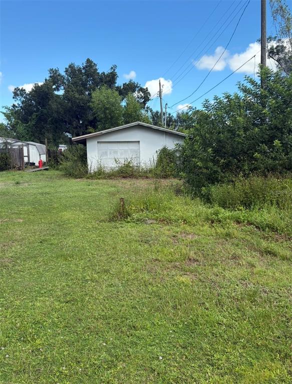 A detached white garage sits on a grassy lot with overgrown vegetation and power lines — 12486 POEM AVENUE, PUNTA GORDA, FL