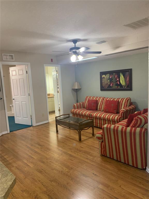 A living room features wood-look flooring, a striped sofa and chair, and two open doorways — 2777 N POINCIANA BOULEVARD UNIT 225A, KISSIMMEE, FL