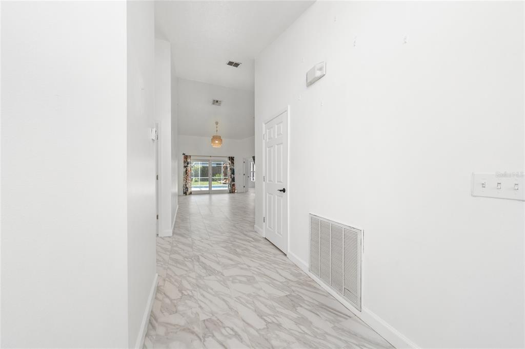 A hallway with white walls and marble-patterned tile flooring leads toward a bright living area — 2608 BRANDYWINE COURT, KISSIMMEE, FL