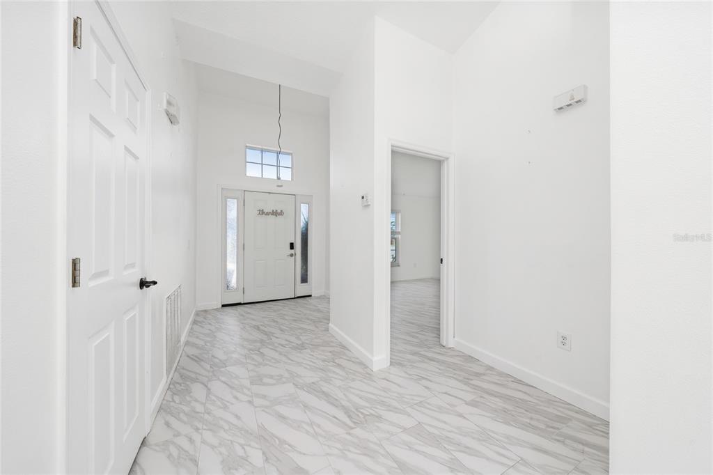 A bright entryway features white walls, high ceilings, and light gray marble-patterned tile flooring — 2608 BRANDYWINE COURT, KISSIMMEE, FL