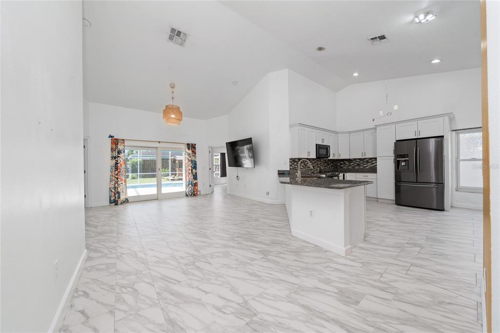 An open-concept kitchen and living area with white cabinets, marble-look tile floors, and sliding doors — 2608 BRANDYWINE COURT, KISSIMMEE, FL