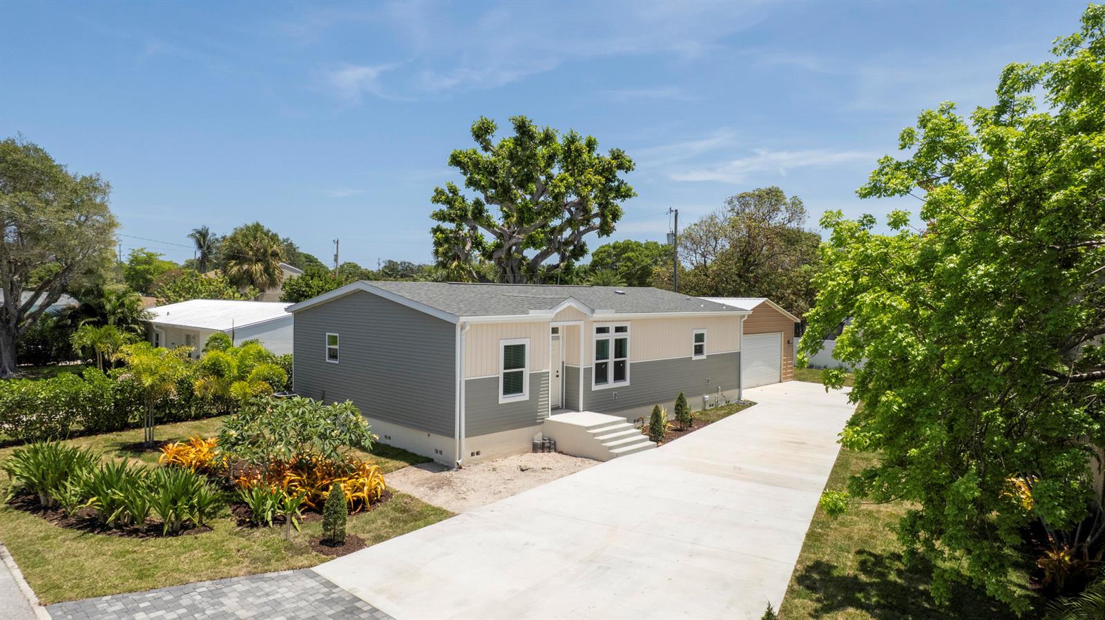A single-story house with two-tone siding and a concrete driveway sits under a blue sky — 1757 N 12th Ct Court N, FL 33460, FL