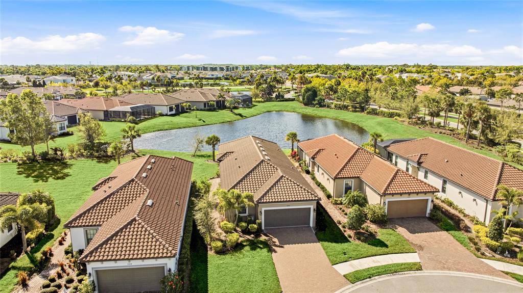An aerial view shows three suburban houses with tiled roofs situated near a small pond — 10414 INGLENOOK TERRACE, PALMETTO, FL