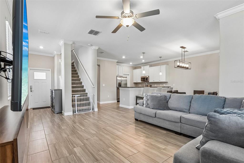 An open-concept living room features wood-look tile flooring, a gray sectional sofa, and a staircase — 17448 RADIANT SHINE WAY, LUTZ, FL
