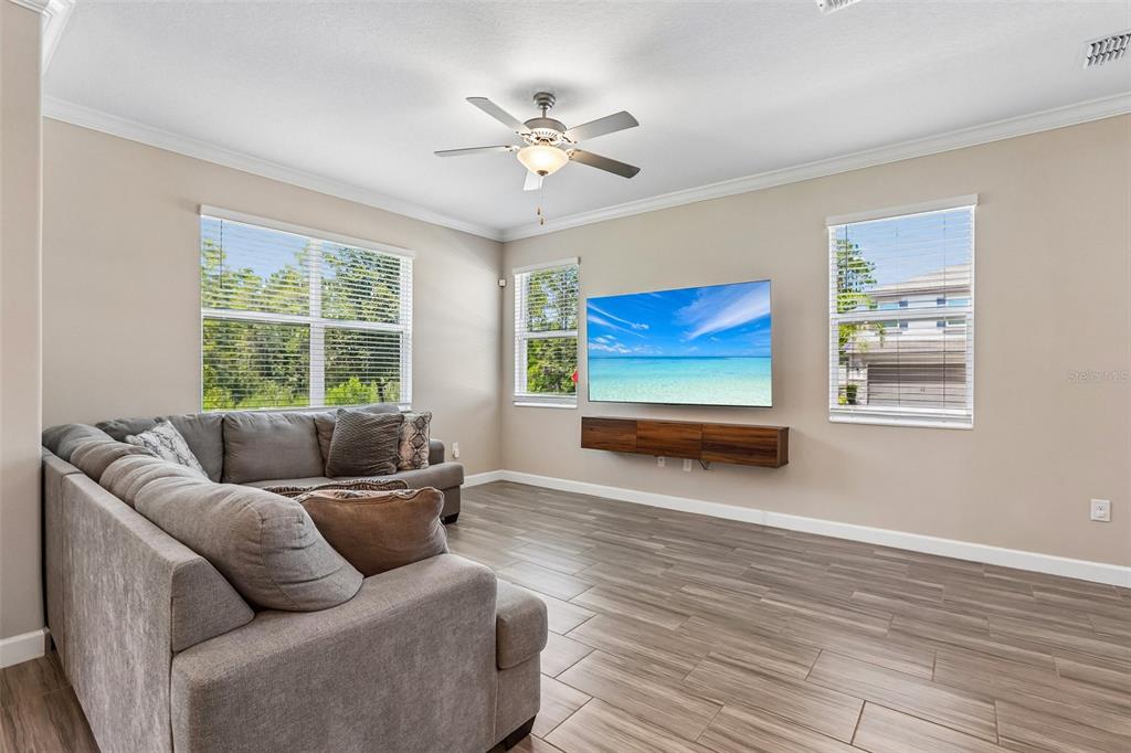 A living room features a gray sectional sofa, a wall-mounted television, and wood-look tile flooring — 17448 RADIANT SHINE WAY, LUTZ, FL